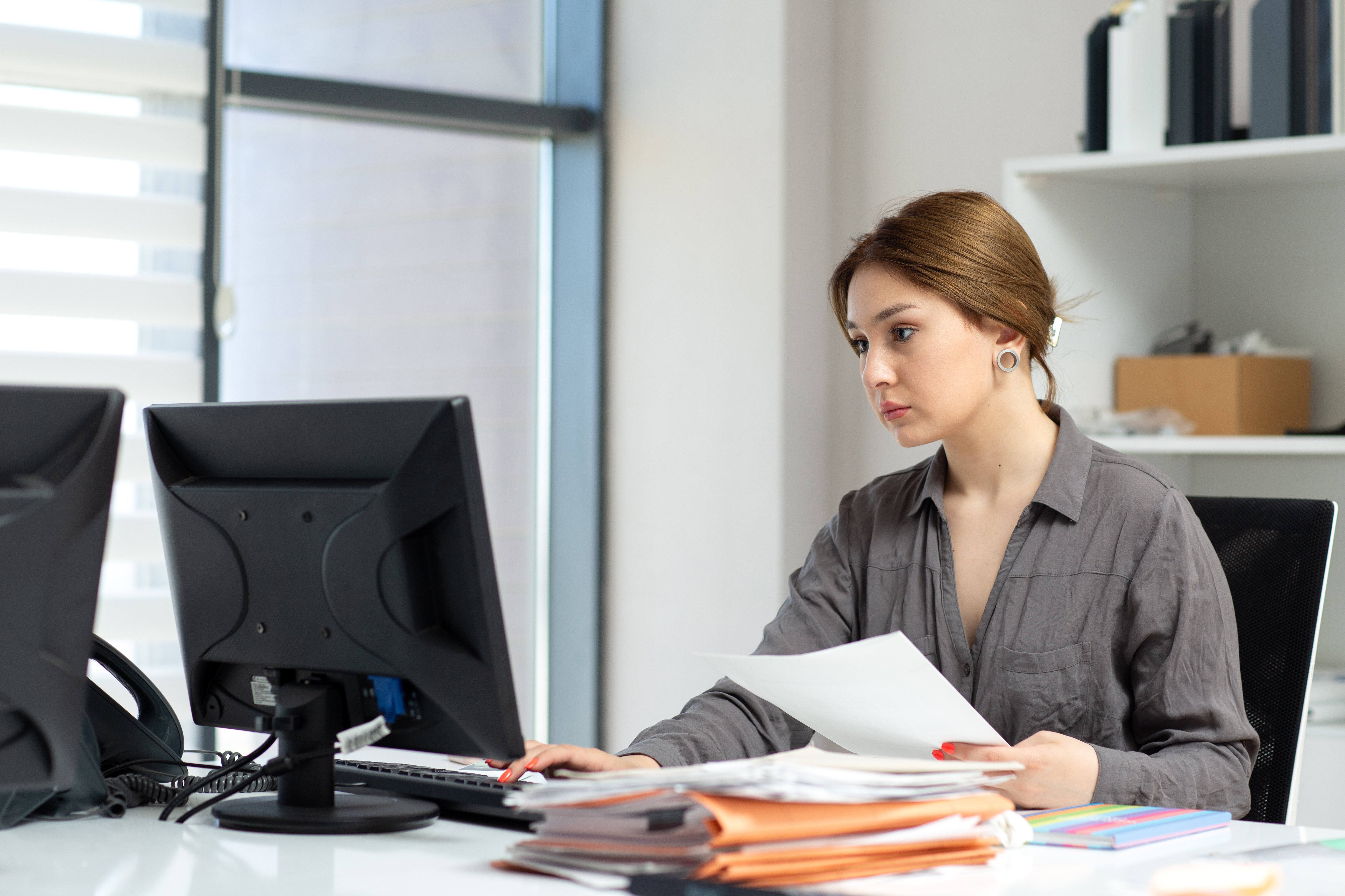 Data entry clerk reviewing documents and entering information into computer in office setting.
